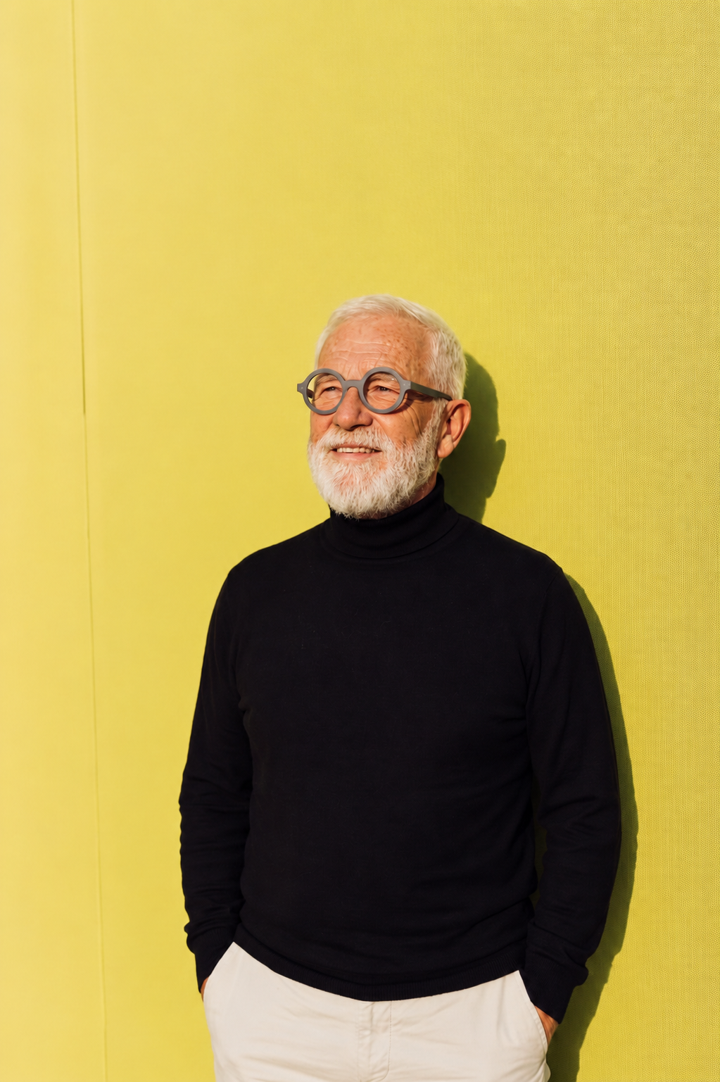 Man with white beard and glasses against a yellow wall